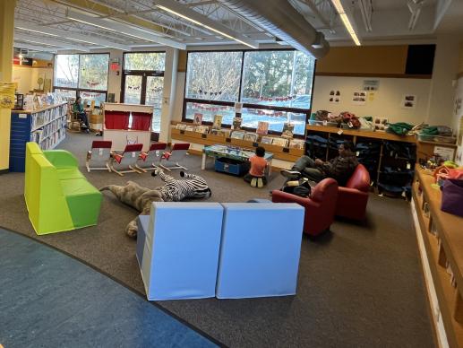 Children's area with soft seating, stuffed animals, puppet theater, train table, and other toys.