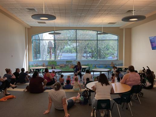 Image of families sitting on the floor together listening to a library worker read a story.