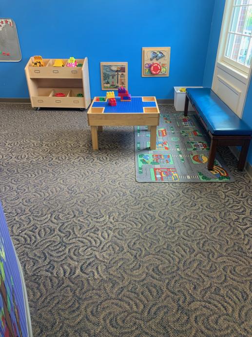 Image of the early childhood play area with a lego table, play vehicles, and sensory wall elements.