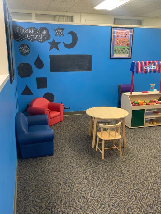 Image of the early childhood play area with dramatic play centers of a market place, dining area, and couch and chair, with kitchen area not pictured.