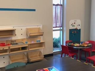 A glimpse of our play kitchen, which includes a small table and four red chairs and wooden kitchen components on the wall. 