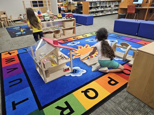 A picture of the play area that includes two children playing with the dollhouse and wooden blocks