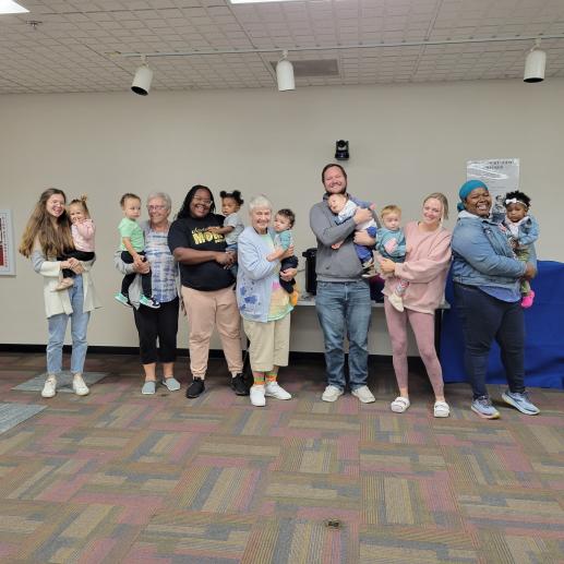 Seven adults pose for a picture, each adult is holding one young child.