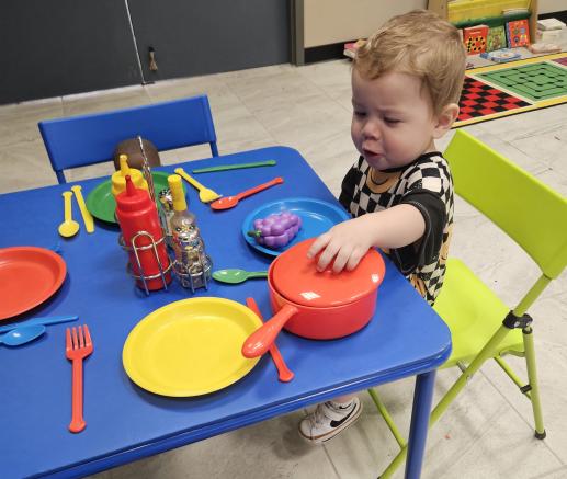 A boy playing pretend with play dishes at a kid's table.