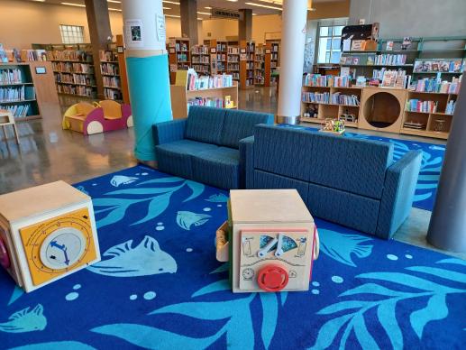 Photograph of part of the Family Place Play area showing couches, play car, manipulatives, and shelves with books in the background