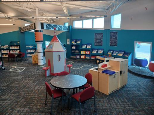 Play area with books, chairs, tables, a bookshelf with toys, and a kitchen set
