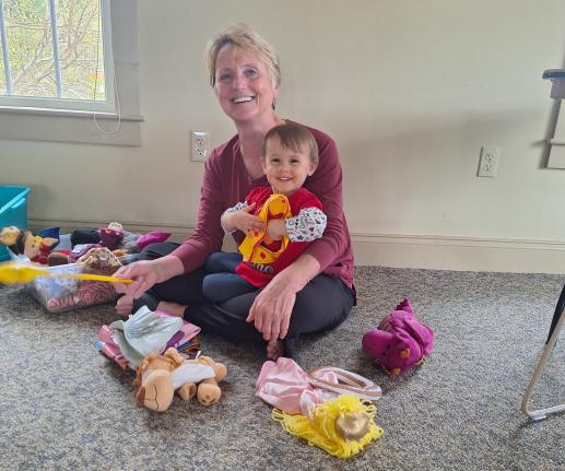A toddler sitting in her grandmother's lap, surrounded by toys, with big smiles on both of their faces