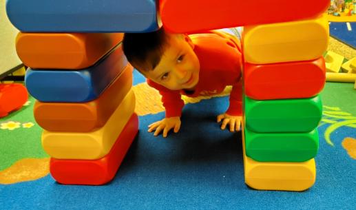 A small child peeks through the tunnel he has built out of oversized locking bricks