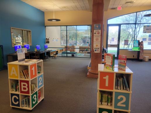 Image of the children's area of a library, with board books, computers, and a play room.