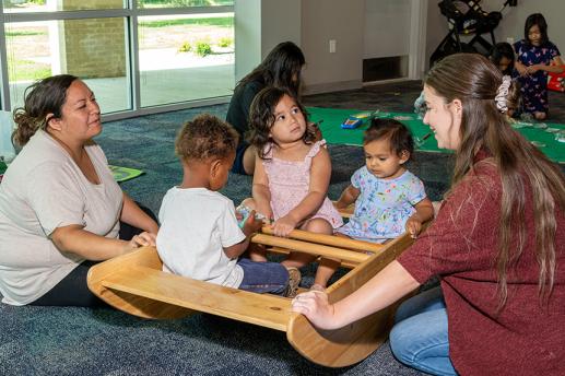 Children sit in a rocking boat while library staff and caregivers look on