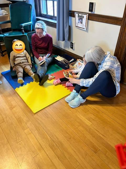 2 adults read a book with a toddler