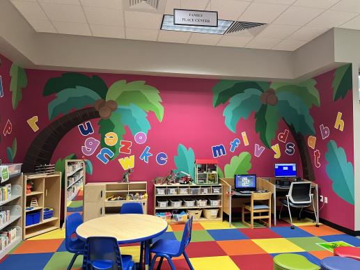 Library children's area with toys and mural with palm trees and the alphabet. 
