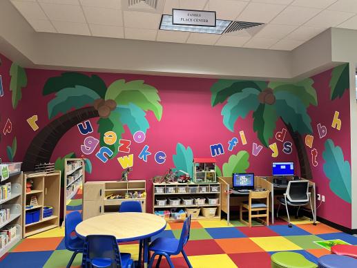 Library children's area with toys and mural with palm trees and the alphabet.