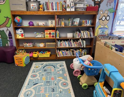 Children's area includes board books, rug, food truck, stroller with a baby doll, grocery cart with a baby doll, Legos, puzzles, dollhouse, vet kit and stacking toys.