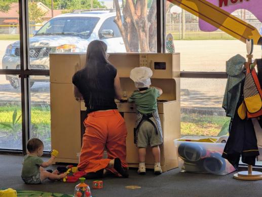 An adult and two young children playing with a toy kitchen.