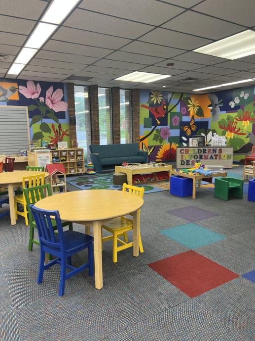 An image out the Marple Library play area, featuring train table, shelves of toys, and Lego table