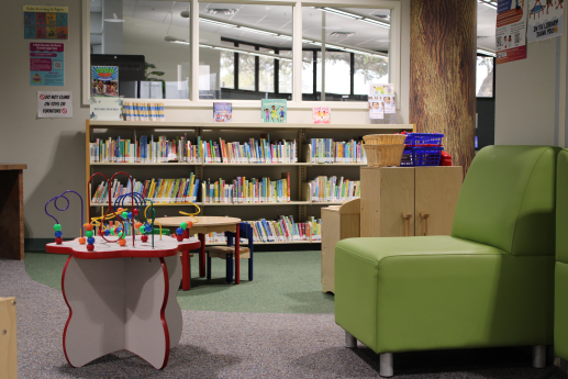 Area has a shelf of board books, kitchen play set, bead table, and green chair.