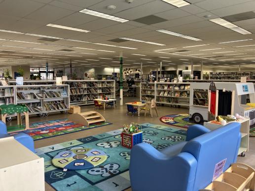 Children's play area in the library with toys, bright carpet, sofas, small tables and toy food truck.