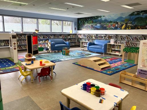 Children's play area in the library. Includes small tables, bright carpets, sofas and toys.