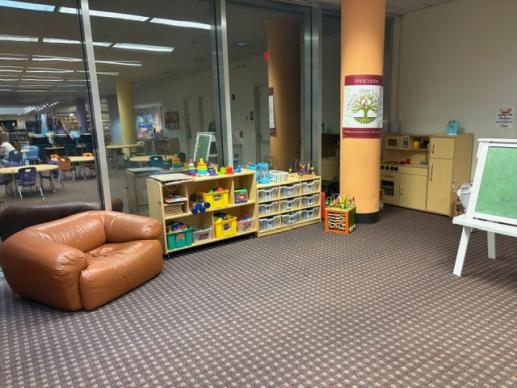 A view of the play area showing an oversized chair, toy storage, a play kitchen and an easel.