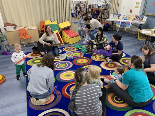 Image of children and caregivers in a circle participating in a music class