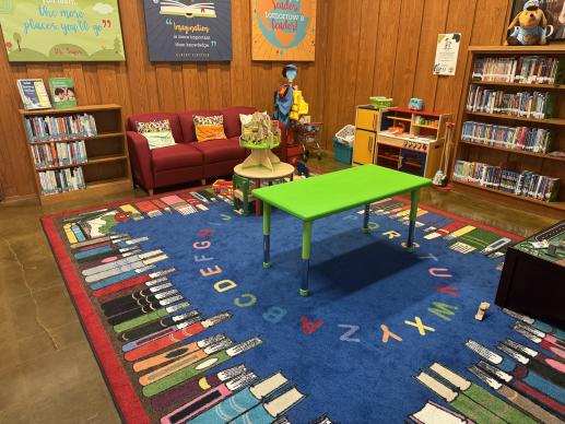 Children's area in the library, with couch, table, play kitchen, and parenting book collection