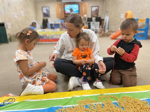 Mother & children stringing noodles onto yarn at the art station during the Parent-Child Workshop.