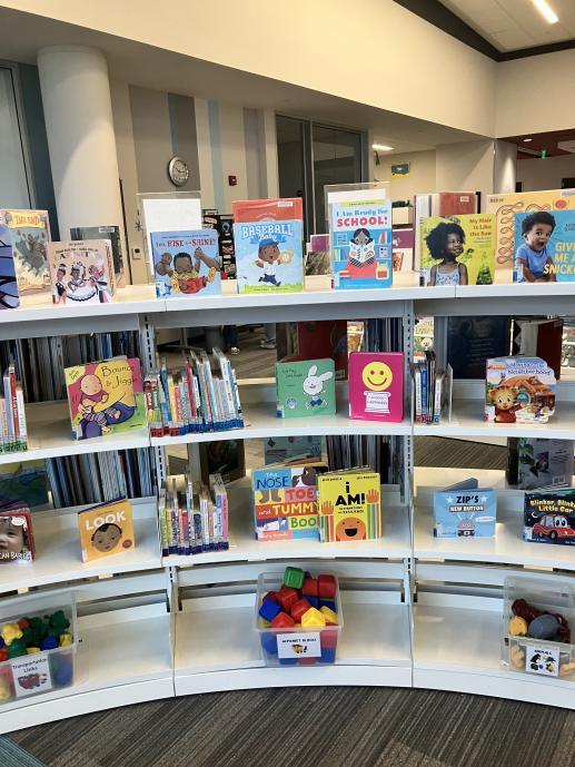 Curved white shelving with colorful board books and plastic totes filled with toys. The toys have picture labels on the front.