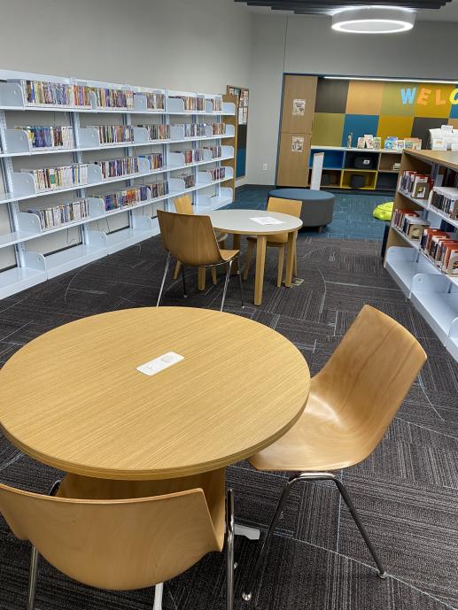 Two tables in a library. Each table has chairs.