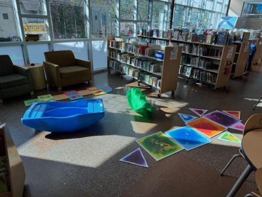 Photo of library shelves with interactive squishy mats and rocking toys in front.