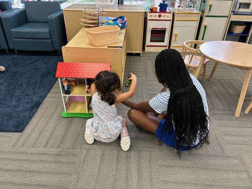 A child and their caretaker play with a dollhouse