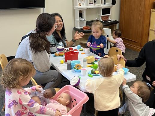 Caregivers chat while playing with their children in the dramatic play area.