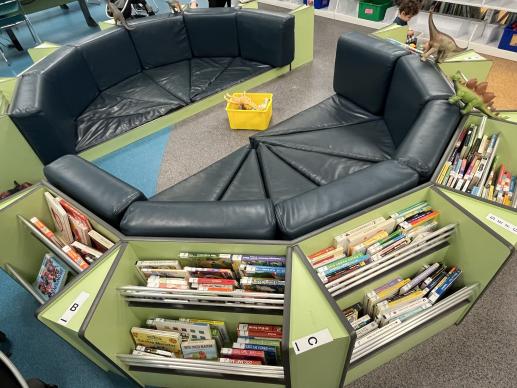 A soft floor-level seating area with attached wooden compartments filled with board books.