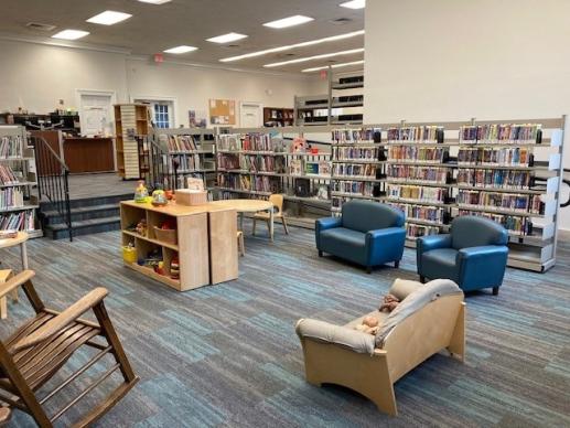 View from the corner of a spacious library area with seating, toys, and children's books.
