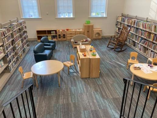 View from the stairs of a spacious library area with seating, toys, and children's books.