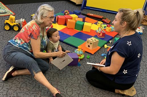 Mom, baby, and older female friend talking and playing in infant toy area.