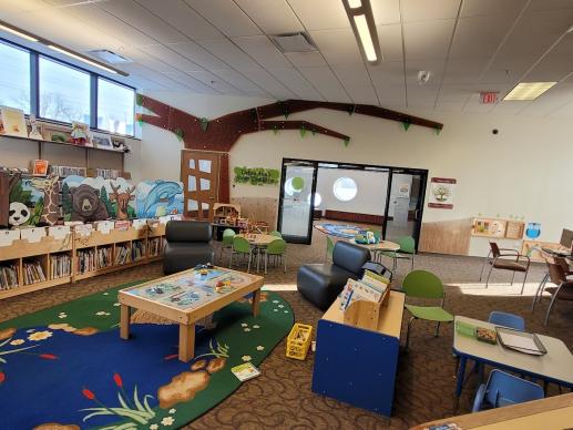 children's area in the library with books, colorful rug, train table, chairs, and toys