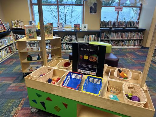 Play marketplace at a library with various market related toys. Books are seen in the background. 