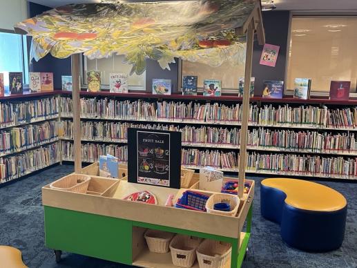A pretend marketplace with market themed toys. Books are in the background. 