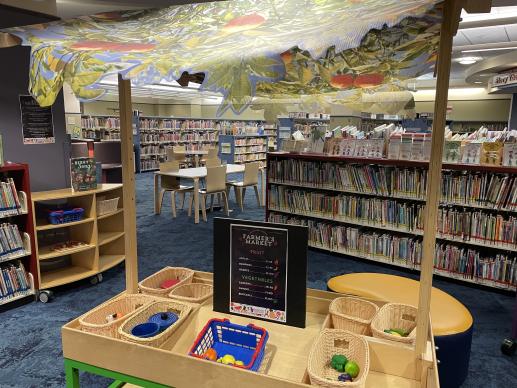 A pretend marketplace with market themed toys. Books are in the background. 
