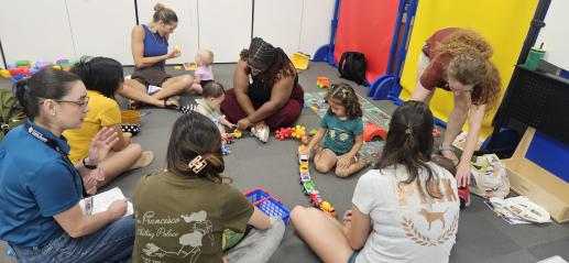 Adults and children sitting on the floor playing with toys during a parent-child workshop. 
