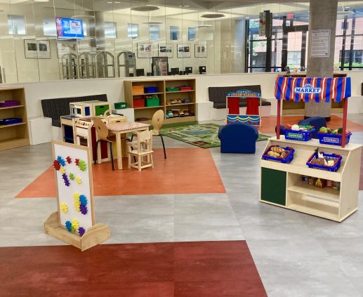 a brightly colored indoor play area for kids, with a magnet board, a farmers market stall, a wooden kitchen, and a puppet theater