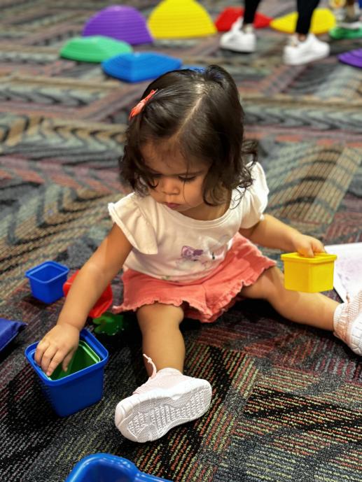 a toddler girl sitting on the floor and playing with brightly colored stacking cups