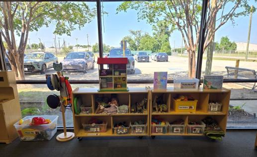 A children's play area in a library. It is colorful, neatly organized, and features many types of toys and dress-up costumes.