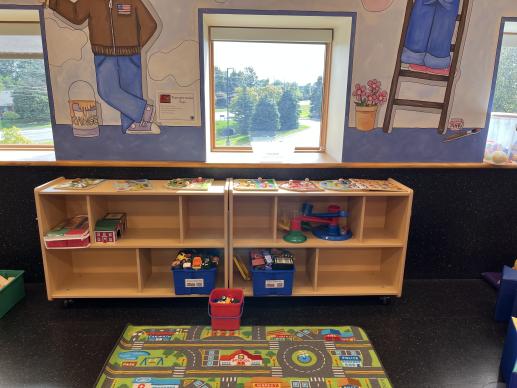 Shelves with bins of toys and a carpet in front with roads on top for kids to play cars and trucks