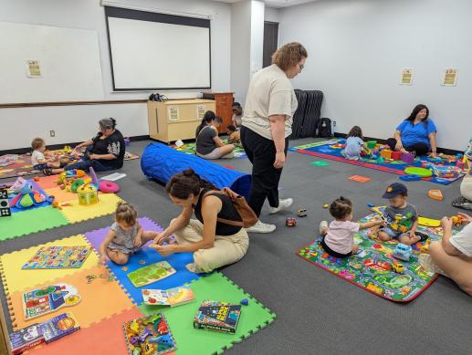 Young children and their caregivers play together in a room with many different types of toys. 