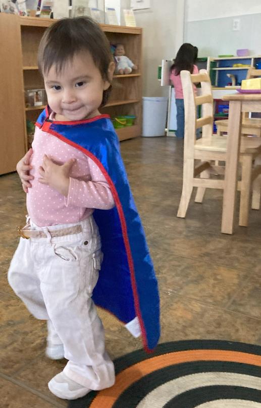 smiling toddler girl wearing blue cape
