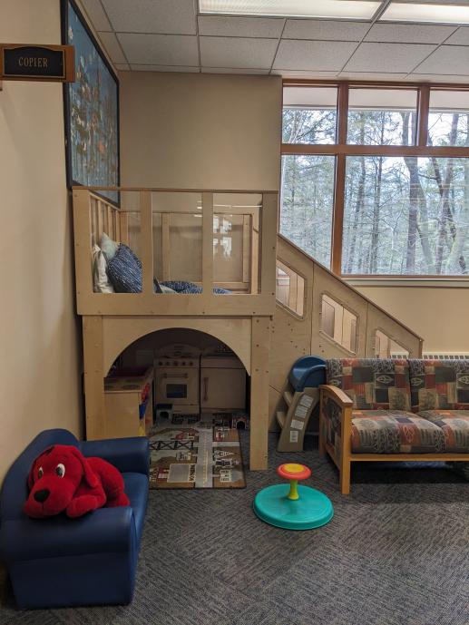 A loft with an open cave underneath. A couch to the right a sit and spin next to it. A blue kid couch to the left with a red clifford stuffed dog sitting on it.