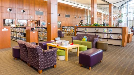 Children’s library space with cozy couches and seating, a play table with building blocks in the foreground, and bookshelves filled with children’s books in the background.
