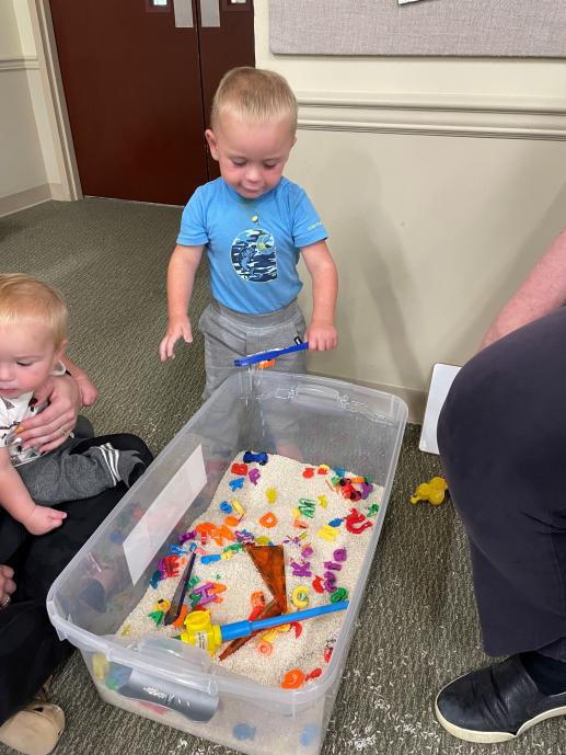 child playing with sensory bin with magnets, rice, and miscellaneous objects